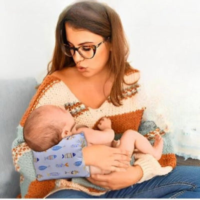 Coussin d’allaitement ergonomique à motif poissons bleus placé sur l’avant-bras d’une maman pour soutenir bébé pendant l’allaitement, offrant confort et position optimale.