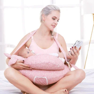 Maman utilisant un coussin d’allaitement rose avec sangle pour allaiter son bébé tout en gardant les mains libres, dans une ambiance détendue à la maison.

