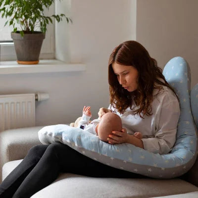 Maman allaitant son bébé confortablement installée avec un coussin de grossesse bleu à motifs étoiles, idéal pour une posture optimale.