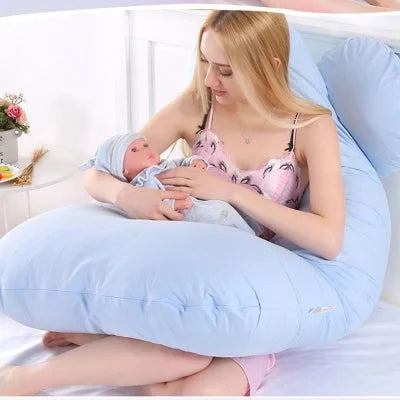 Jeune maman tenant son bébé dans les bras tout en étant soutenue par un coussin de grossesse bleu pastel, parfait pour l’allaitement et le cocooning.