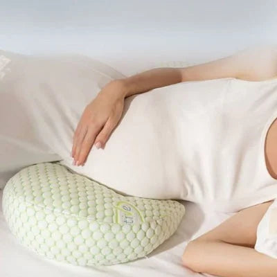 Zoom sur le coussin de grossesse positionné sous le ventre d’une future maman pour soulager la pression abdominale pendant le sommeil.