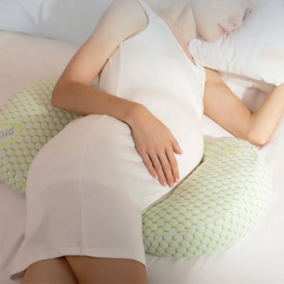 Femme enceinte dormant paisiblement sur le côté avec un coussin de grossesse ergonomique vert pastel à motifs alvéolés.