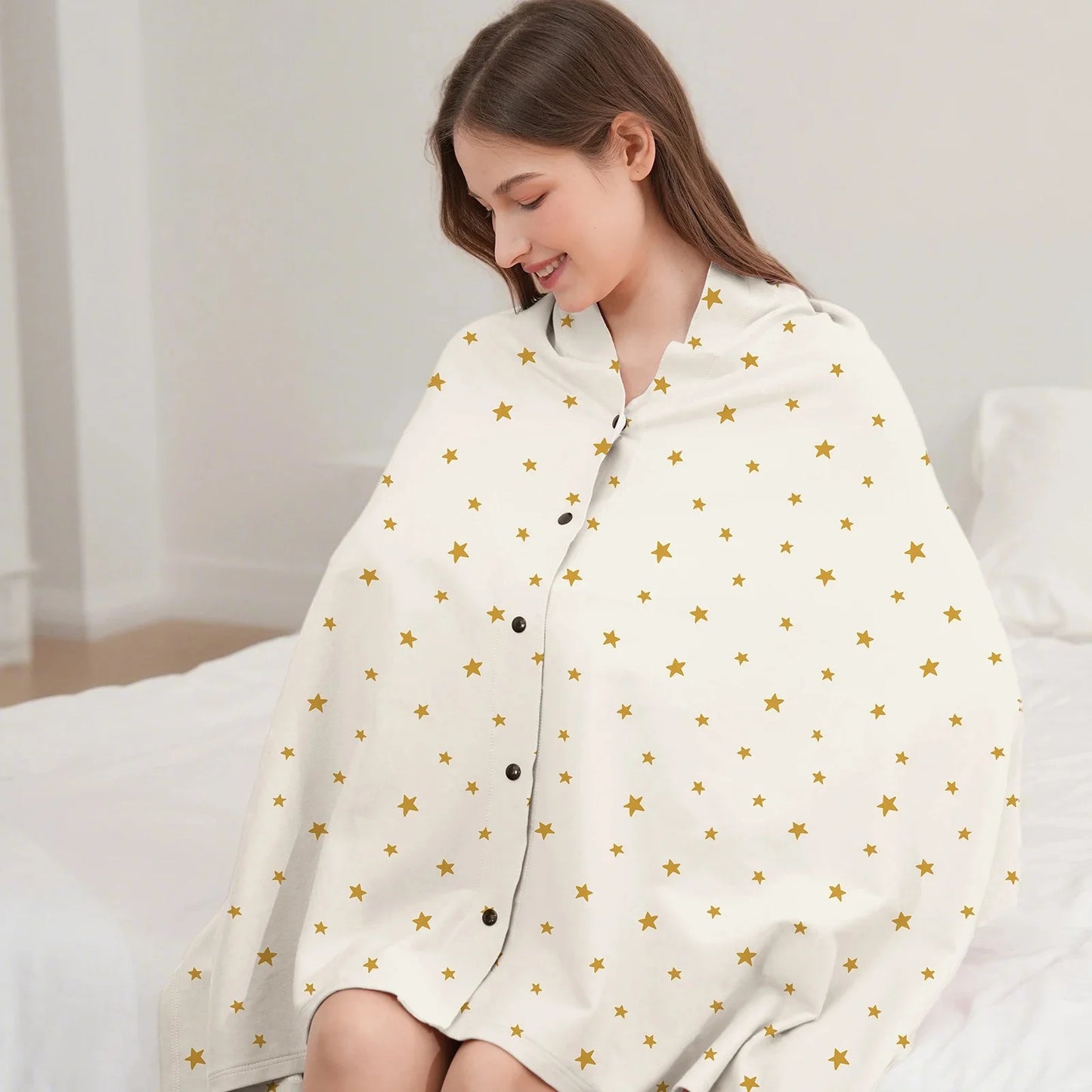 Écharpe d'allaitement DouxVoile blanc cassé étoiles dorées portée en couverture sur lit — boutons pression noirs, coupe enveloppante