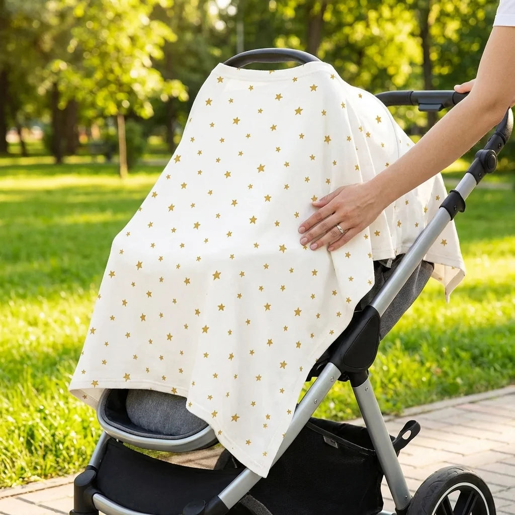 Écharpe d'allaitement DouxVoile crème étoiles dorées utilisée comme protection soleil sur poussette dans parc — main de maman ajuste le tissu