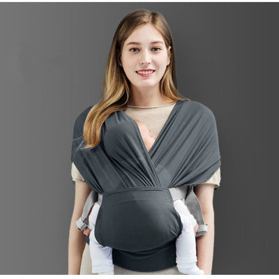 Jeune maman souriante portant son bébé en position kangourou avec une écharpe de portage gris foncé.

