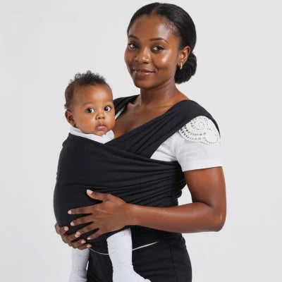 Maman souriante tenant bébé en écharpe de portage noire, posture droite favorisant le contact peau à peau et l’éveil du bébé.