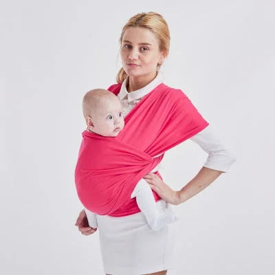 Maman debout portant bébé en écharpe de portage rose, position ventrale latérale pour allaitement pratique et mains libres.
