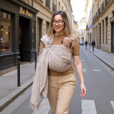 Jeune maman marchant en ville avec son bébé dans une écharpe de portage sans nœud beige, portage ventral physiologique et sécurisé.