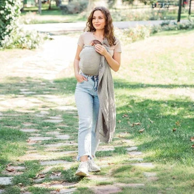 Maman marchant dans un parc avec bébé installé dans une écharpe de portage sans nœud grise, portage physiologique et mains libres.