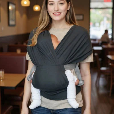 Maman portant son bébé en écharpe de portage dans un café, montrant l’usage pratique au quotidien.