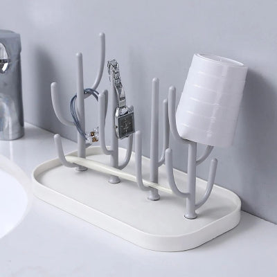 Support biberon utilisé comme rangement multifonction pour montres, bracelets et gobelets, illustrant sa polyvalence dans une salle de bain.