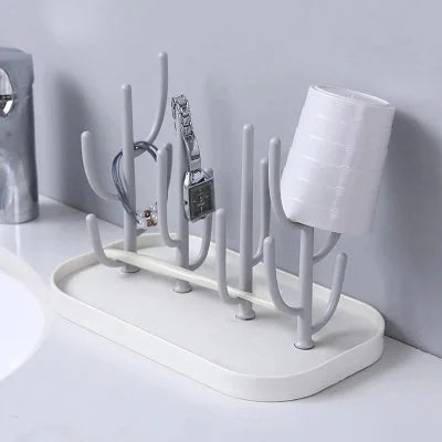 Support biberon utilisé comme rangement multifonction pour montres, bracelets et gobelets, illustrant sa polyvalence dans une salle de bain.