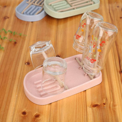 Égouttoir biberon rose pastel sur plan de travail, avec bouteilles en verre et tétines positionnées pour un séchage rapide et organisé.