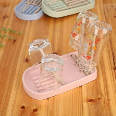 Égouttoir biberon rose pastel sur plan de travail, avec bouteilles en verre et tétines positionnées pour un séchage rapide et organisé.