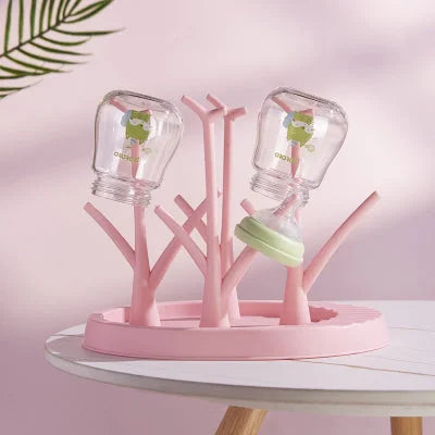 Égouttoir biberon rose pastel en usage, équipé de deux biberons et une tétine, parfait pour une organisation hygiénique et esthétique du coin repas bébé.

