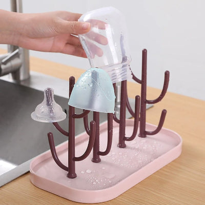 Support biberon en cours de séchage avec des gouttes d’eau visibles sur les accessoires, montrant l’efficacité du drainage et l’hygiène assurée.