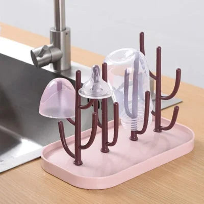 Égouttoir biberon rose et brun utilisé en cuisine, supportant un biberon, une tétine et un capuchon après lavage, parfait pour maintenir l’hygiène bébé.