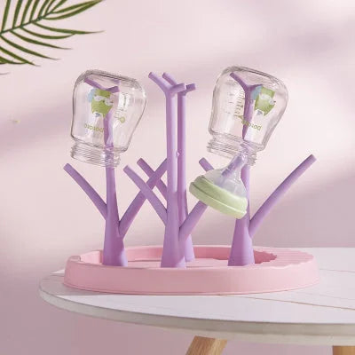 Égouttoir biberon violet avec plateau rose, séchant deux biberons et une tétine dans une ambiance douce et organisée, parfaite pour les jeunes parents.

