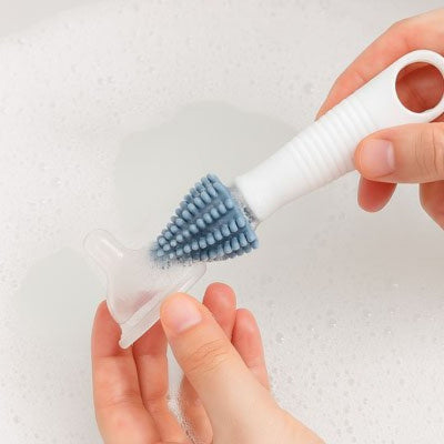 Mini goupillon en silicone bleu nettoyant une tétine de biberon, accessoire pratique pour l’hygiène quotidienne des bébés.