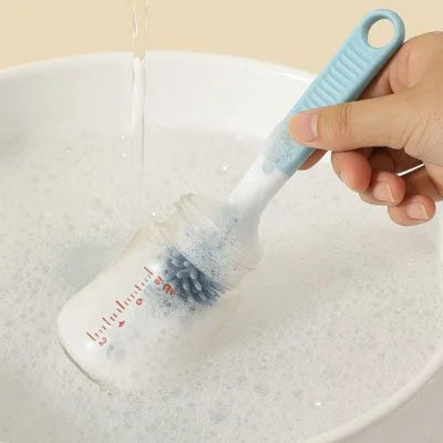 Goupillon pour biberon en silicone bleu utilisé pour nettoyer l’intérieur d’un biberon rempli de mousse savonneuse.