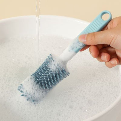Goupillon pour biberon en silicone bleu utilisé dans un bol rempli de mousse, brosse à biberon efficace pour un nettoyage en profondeur et hygiénique.