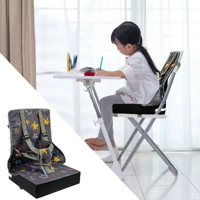 Fille assise sur un coussin réhausseur chaise enfant, utilisant le rehausseur de chaise bébé comme coussin surelevateur pour écrire à la table.