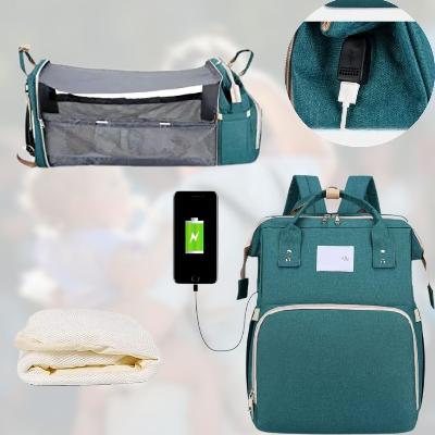 Sac à dos à langer AllDay Comfort vert forêt avec port USB, station à langer intégrée et matelas confortable. Présenté avec un téléphone en charge, idéal pour des parents modernes et connectés