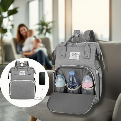 Sac à dos à langer AllDay Comfort gris douceur avec poches imperméables, port USB et 15 compartiments. Présenté dans un salon lumineux avec une maman tenant son bébé, parfait pour un style polyvalent et pratique.