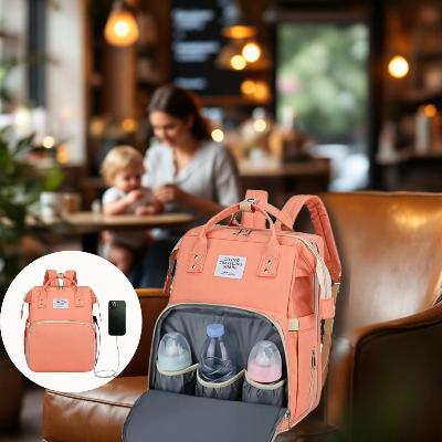 Sac à dos à langer AllDay Comfort couleur rose crépuscule avec poches isothermes, port USB et matelas à langer intégré. Présenté dans un café cosy avec une maman et son enfant, idéal pour des sorties élégantes et organisées.