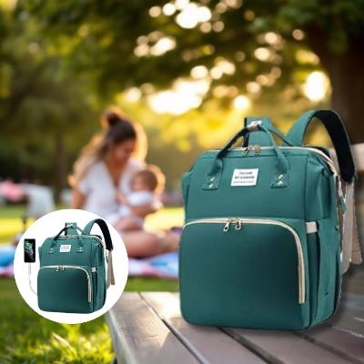 Sac à dos à langer AllDay Comfort vert forêt, doté de compartiments multiples, poches isothermes et port USB. Photographie dans un parc ensoleillé avec une maman et son bébé, parfait pour des aventures en plein air