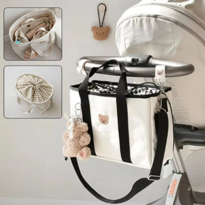 Sac à langer blanc avec attache poussette pratique, accompagné d’un charm ourson et de multiples compartiments, conçu pour faciliter la vie des parents actifs.