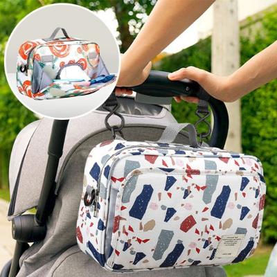 Sac à langer bébé HappyNest™ à motifs terrazzo, suspendu à une poussette, pour des sorties confortables et modernes.