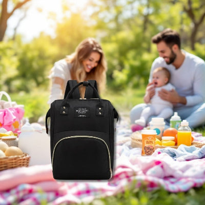 Sac à langer bébé noir avec poches multiples, présenté lors d’un pique-nique familial en plein air, mettant en avant sa praticité pour transporter les affaires essentielles de bébé.