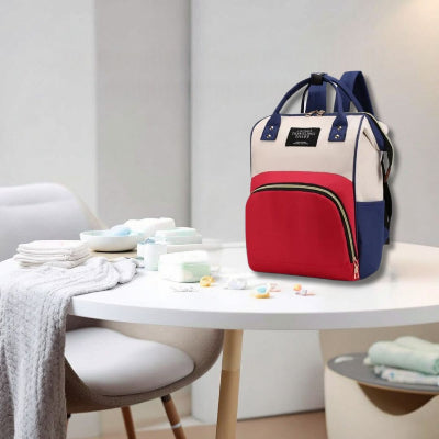 Sac à langer bébé Rouge Élégance posé sur une table à langer, entouré de produits essentiels pour bébé. Design élégant avec grande capacité et poches pratiques.