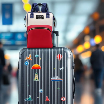 n sac à langer bébé rouge et bleu marine posé sur une élégante valise argentée dans un terminal d’aéroport, mettant en avant son design pratique et adapté aux voyages.