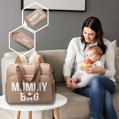 Une maman assise dans son salon avec son bébé, utilisant un sac à langer Beige Chic, accompagné de ses pochettes assorties pour un rangement optimal à la maison.