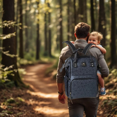 Sac à dos à langer bleu profond avec poches isothermes, porté par un père lors d'une randonnée en forêt avec son enfant, illustrant sa praticité et confort.