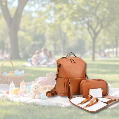 Sac à langer Caramel Chic dans un parc lors d’un pique-nique familial, avec ses accessoires et un grand espace pour les essentiels de bébé.