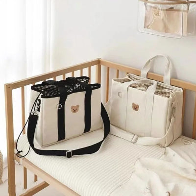 Deux sacs à langer "Ourson Tendre" en noir et blanc posés sur un lit d'enfant dans une chambre lumineuse, parfaits pour organiser les essentiels de bébé.