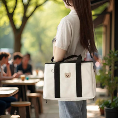 Sac à langer noir et blanc porté en bandoulière dans un cadre urbain convivial avec des cafés en arrière-plan, parfait pour des sorties élégantes avec bébé.