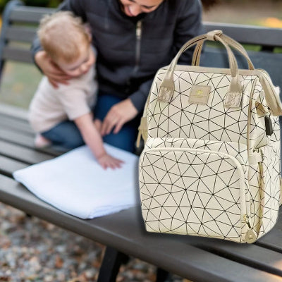 Sac à dos à langer Champagne Lumière posé sur un banc au parc, avec une maman et son bébé profitant d’un moment familial chaleureux.