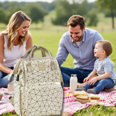 Famille heureuse profitant d’un pique-nique en plein air, le sac à dos à langer Champagne Lumière en avant-plan, mettant en avant son style moderne et son organisation efficace.