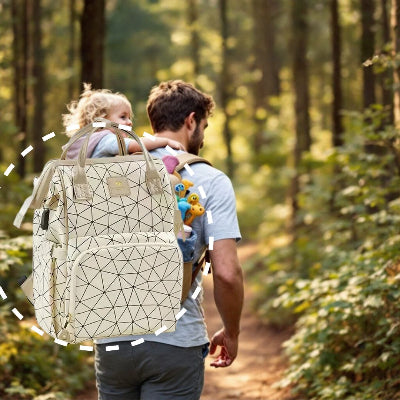 Papa portant sa fille sur le dos tout en utilisant le sac à dos à langer Champagne Lumière pour une randonnée en forêt, soulignant sa grande capacité et son confort.