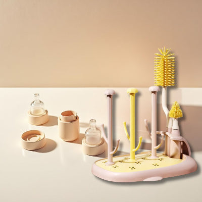 Sèche biberon CleanDrop™ rose et jaune accompagné de tétines, bagues et capuchons disposés sur le plan de travail, parfait pour le séchage rapide et hygiénique.

