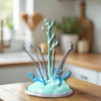 Sèche biberon design en forme d’arbre vert menthe et gris, posé sur un plan de travail en bois dans une cuisine lumineuse, idéal pour sécher biberons et tétines tout en gardant l’espace propre et organisé.

