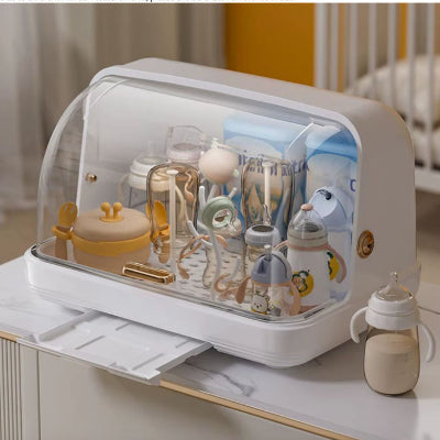 Sèche biberon BibStand™ avec bac récupérateur d’eau en position ouverte, installation sur plan de travail dans une chambre de bébé moderne.

