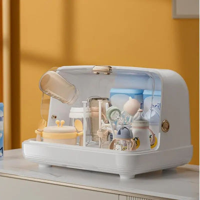 Sèche biberon blanc ouvert contenant des biberons, cuillères, tétines et contenants alimentaires dans un environnement lumineux et soigné.