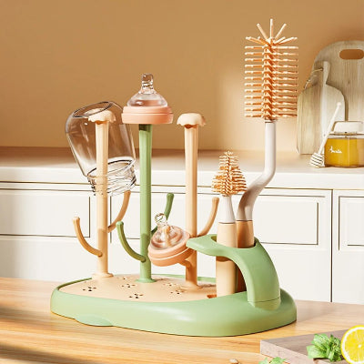 Sèche biberon CleanDrop™ vert et beige avec brosses intégrées et biberons en cours de séchage sur un plan de travail en bois clair dans une cuisine moderne.


