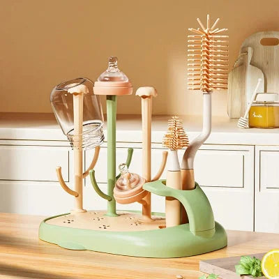 Sèche biberon CleanDrop™ vert et beige avec brosses intégrées et biberons en cours de séchage sur un plan de travail en bois clair dans une cuisine moderne.

