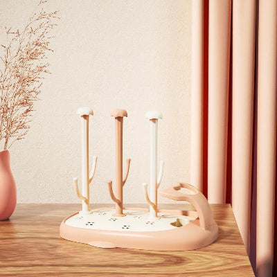 Sèche biberon CompactBébé™ en teinte pêche, avec tiges longues et design épuré, posé sur un plan de travail en bois clair dans une cuisine au décor chaleureux, idéal pour sécher les biberons et accessoires tout en optimisant l’espace.